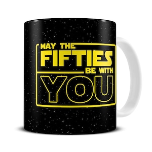 May include: Black ceramic mug with a white handle. The mug features the text "MAY THE FIFTIES BE WITH YOU" in yellow, set against a starry background. A fun, pop culture themed mug.