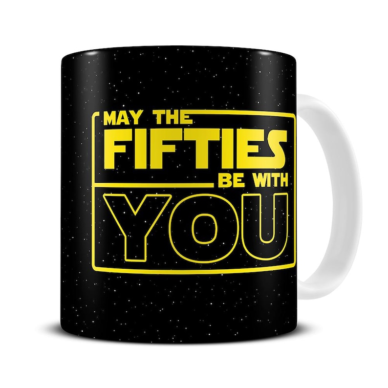 May include: Black ceramic mug with a white handle. The mug features the text "MAY THE FIFTIES BE WITH YOU" in yellow, set against a starry background. A fun, pop culture themed mug.
