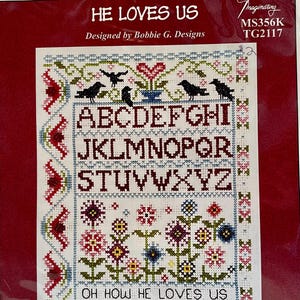 May include: Cross-stitch kit with the text "HE LOVES US" and "OH HOW HE LOVES US". The design features an alphabet, flowers, birds, and decorative borders in red, blue, green, and white. The kit is designed by Bobbie G. Designs.