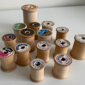 May include: A collection of vintage wooden spools with various labels. The spools are in shades of light brown and beige, with labels featuring text like "COATS & CLARKS" and "STAR MERCERIZED". Some labels have red, blue, and pink accents.