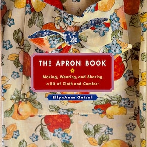 May include: The Apron Book cover. The book features a red and white framed title with the text "THE APRON BOOK" and the subtitle "Making, Wearing, and Sharing a Bit of Cloth and Comfort". The cover has a floral pattern with apples and pears.