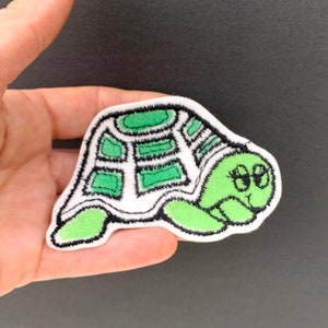 May include: Green embroidered iron-on patch of a cartoon turtle with big eyes.