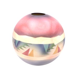 May include: A spherical glass vase featuring a smooth, rounded silhouette with a small circular opening at the top. The surface displays a gradient of soft pink, cream, and blue hues, accented by a band of small, colourful geometric triangle patterns.