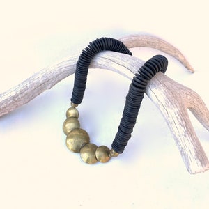 以下が含まれることがあります： 黒いビーズのネックレスに、大きな金の円盤形のペンダントがついたもの。ネックレスは白い鹿の角の上に置かれています。