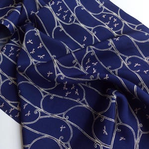 May include: Navy blue fabric featuring a repeating pattern of white bird and scroll motifs. The fabric is folded, revealing its texture and depth. The design is elegant and decorative, suitable for various textile projects. The fabric is in a folded state.