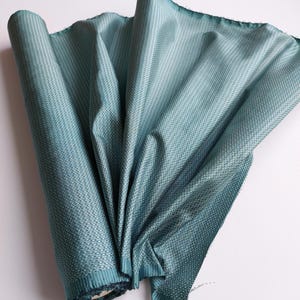 Peut inclure: Un rouleau de tissu bleu sarcelle avec un motif tissé texturé. Le tissu est plié et roulé.