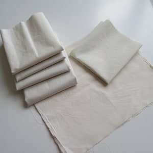 Peut inclure: Une pile de cinq carrés de tissu blanc, un seul carré de tissu blanc et un grand carré de tissu blanc.