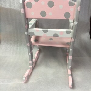May include: A pink and gray rocking chair with a polka dot pattern. The chair is made of wood and has a rounded back.