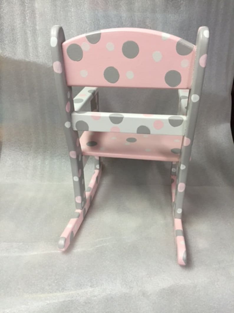 May include: A pink and gray rocking chair with a polka dot pattern. The chair is made of wood and has a rounded back.