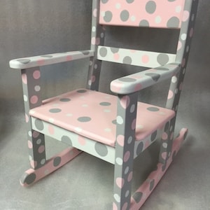 May include: A pink and gray rocking chair with a polka dot pattern. The chair is made of wood and has a rounded back.