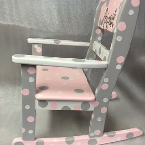 May include: A gray and pink rocking chair with white polka dots. The chair is personalized with the name "Abigail" on the back.
