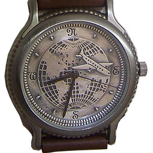 May include: A silver-toned wristwatch with a brown leather band. The watch face features a world map with an airplane flying over it. The numbers 12, 3, 6, and 9 are visible on the watch face.