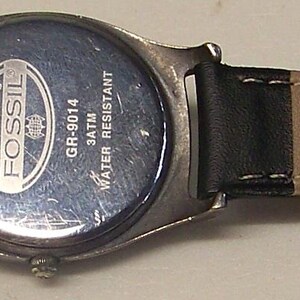 May include: A Fossil brand wristwatch with a black leather band and a silver-toned case. The watch band is tan on the inside. The watch is water resistant.
