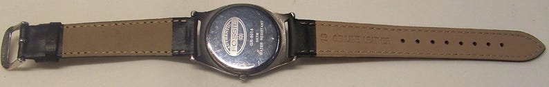 May include: A Fossil brand wristwatch with a black leather band and a silver-toned case. The watch band is tan on the inside. The watch is water resistant.