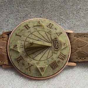May include: A brown leather wristwatch with a round, copper-colored face. The face features a sundial design with Roman numeral markings and the word "FOSSIL" inscribed.