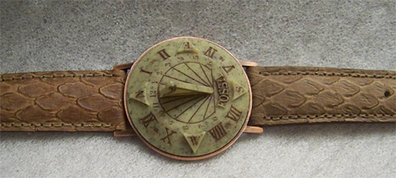 May include: A brown leather wristwatch with a round, copper-colored face. The face features a sundial design with Roman numeral markings and the word "FOSSIL" inscribed.