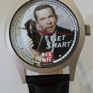 May include: A silver wristwatch with a black leather band. The watch face features a color image of Don Adams as Maxwell Smart from the TV show "Get Smart". The watch face also includes the text "Get Smart" and "Nick at Nite Classic TV".