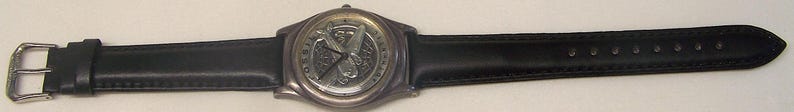 May include: A wristwatch with a black leather band and a silver-toned watch face. The watch face features a detailed design. The band is secured with a silver buckle.
