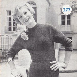 May include: A black and white photo of a woman wearing a tailored dress in boucle. The dress is a simple, fitted style with a high neckline. The woman is standing in front of a building with a window and a balcony. The image includes the text "PATTERN M201/277 TAILORED DRESS IN BOUCLET FOR USE ON THE PASSAP M201 HANDKNITTING MACHINE 6d".