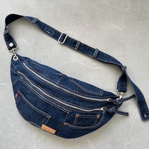 Può includere: Una borsa a tracolla in denim blu scuro con più scomparti con cerniera e una lunga tracolla regolabile.