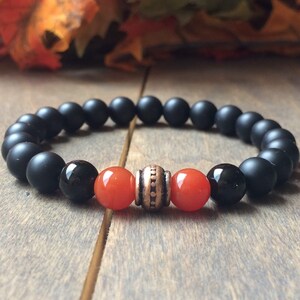 A black beaded bracelet with two orange carnelian beads and a copper spacer bead.