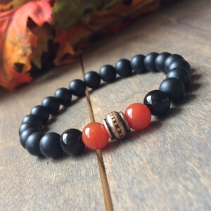 A black matte beaded bracelet with two orange carnelian beads and a copper spacer bead.