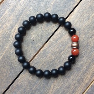 A black matte beaded bracelet with two orange carnelian beads and a copper spacer bead.