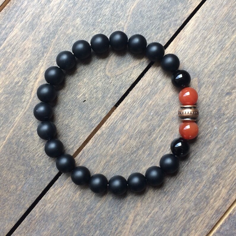 A black matte beaded bracelet with two orange carnelian beads and a copper spacer bead.