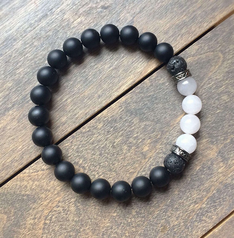 May include: A black and white beaded bracelet with black lava rock beads and white agate beads. The bracelet has silver metal accents.