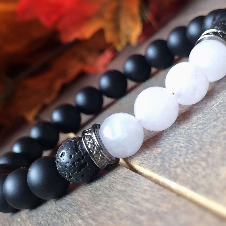 May include: A black and white beaded bracelet with silver accents. The bracelet features black matte beads, white beads, and a lava rock bead with a silver accent.