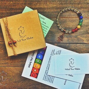 May include: A clear crystal bracelet with a hamsa charm and seven chakra colored beads. The bracelet is packaged in a brown box with the text "Unlock Your Chakra" on it. There are also two cards with the same text and a diagram of the seven chakras.