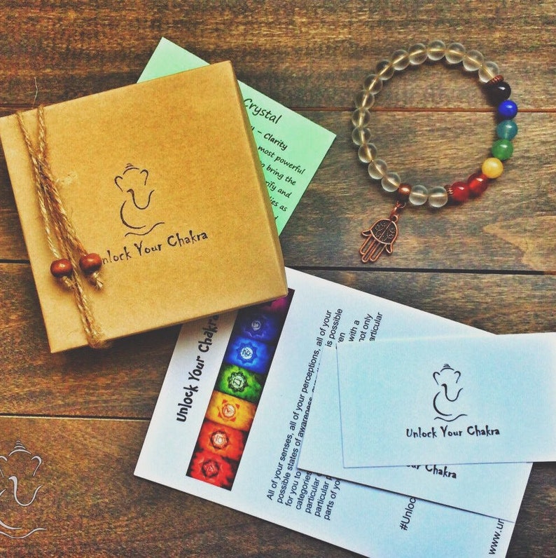 May include: A clear crystal bracelet with a hamsa charm and seven chakra colored beads. The bracelet is packaged in a brown box with the text "Unlock Your Chakra" on it. There are also two cards with the same text and a diagram of the seven chakras.