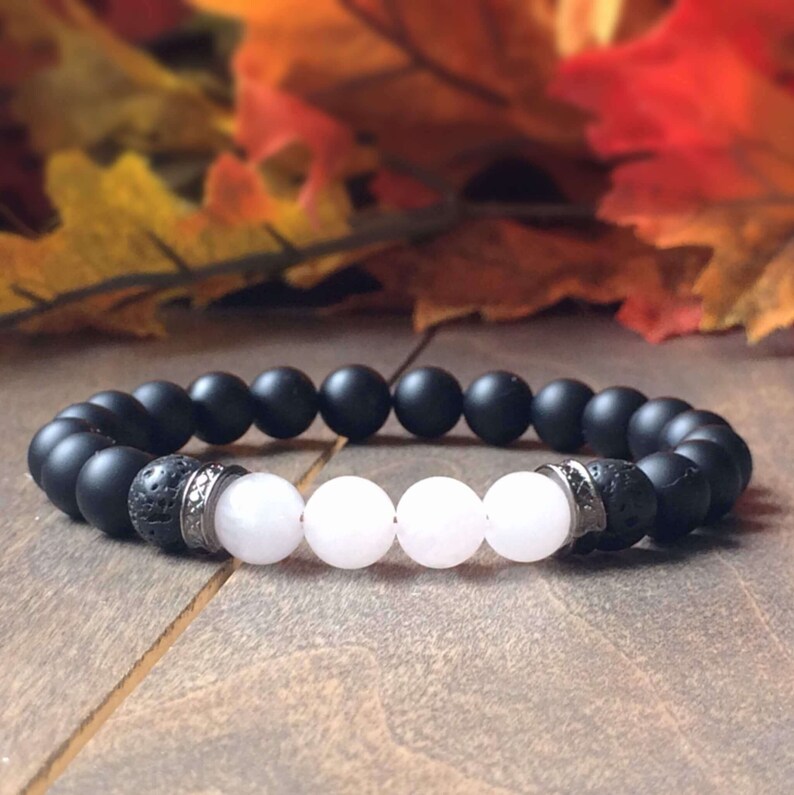 May include: A black and white beaded bracelet with lava rock beads and silver accents. The bracelet has a minimalist design and is made with natural stones.