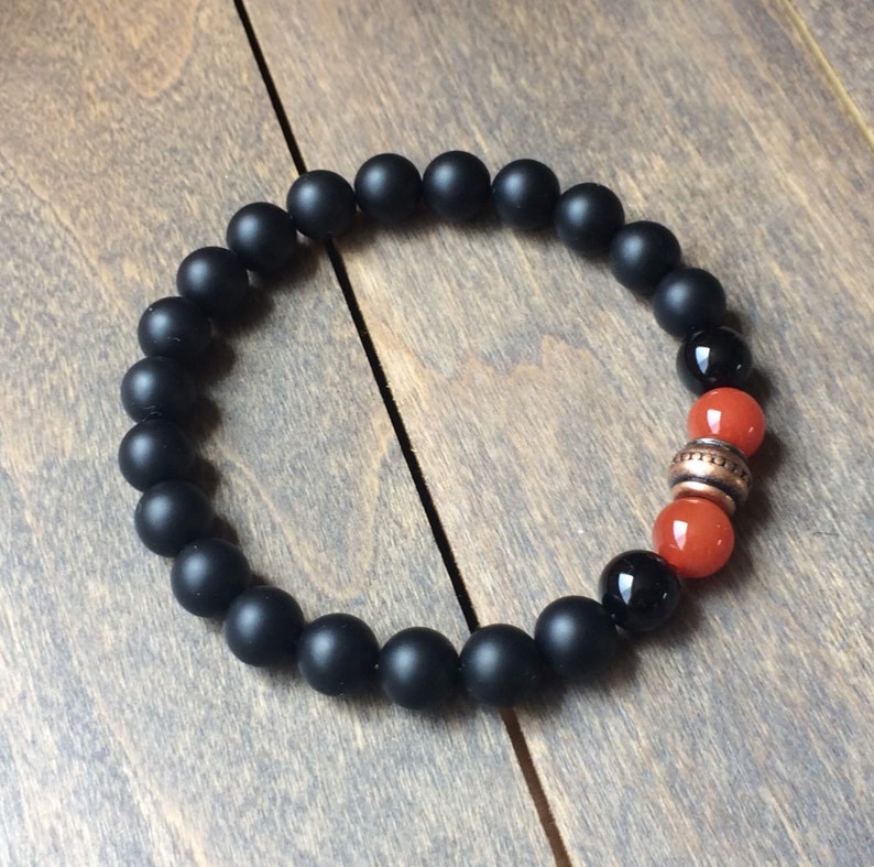 A black beaded bracelet with two orange carnelian beads and a copper spacer bead.