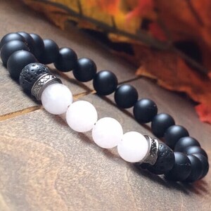 May include: A black and white beaded bracelet with a silver accent. The bracelet features black matte beads, white beads, and a silver spacer bead.