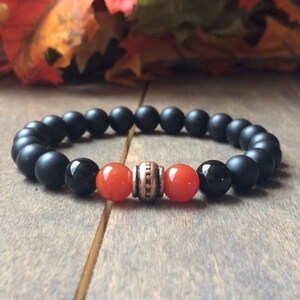 A black matte beaded bracelet with two orange carnelian beads and a copper spacer bead.