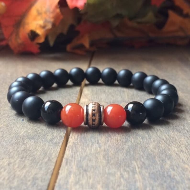 A black matte beaded bracelet with two orange carnelian beads and a copper spacer bead.