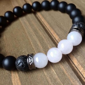 May include: A black and white beaded bracelet with a silver accent. The bracelet features black onyx, lava rock, and rose quartz beads.