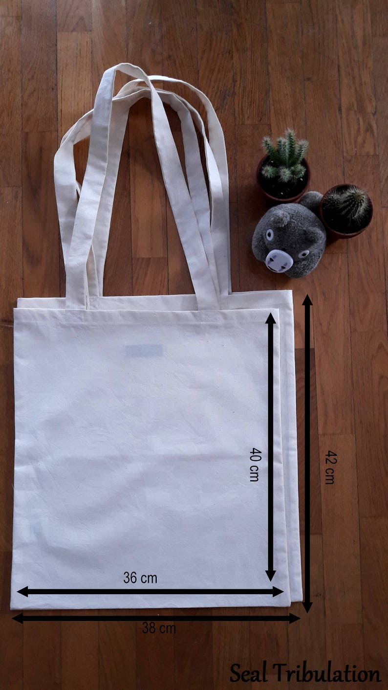 Op de afbeelding: Een blanco canvas draagtas, 36 cm breed en 40 cm hoog, met lange handvatten. De tas is gemaakt van een lichtgekleurde stof. De totale hoogte van de tas is 42 cm. De tekst "Seal Tribulation" staat onderaan.