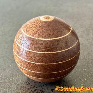 May include: A wooden sphere with a brown and light brown striped pattern. The sphere is smooth and polished.
