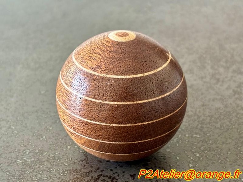 May include: A wooden sphere with a brown and light brown striped pattern. The sphere is smooth and polished.