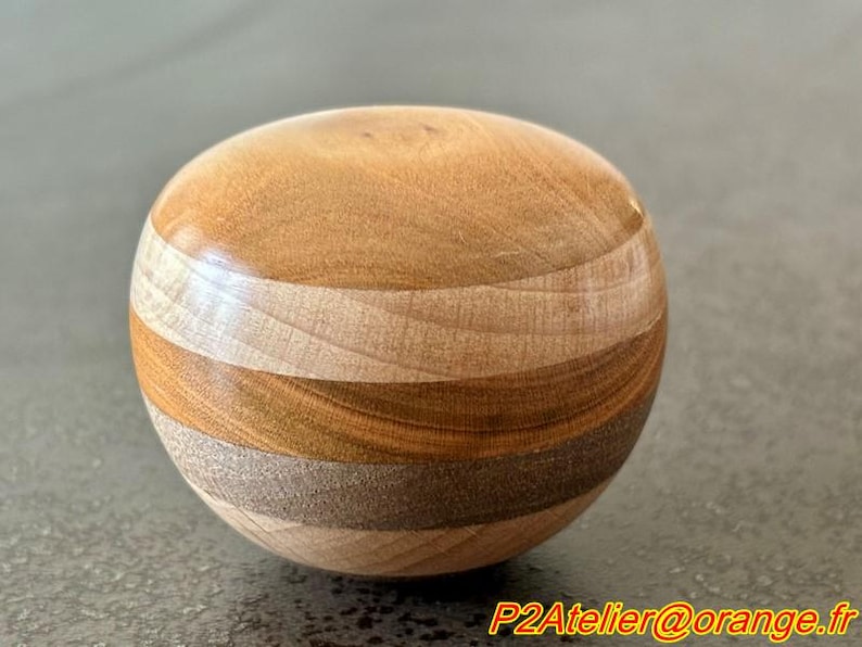 May include: A wooden sphere with a layered design, featuring alternating bands of light and dark wood.