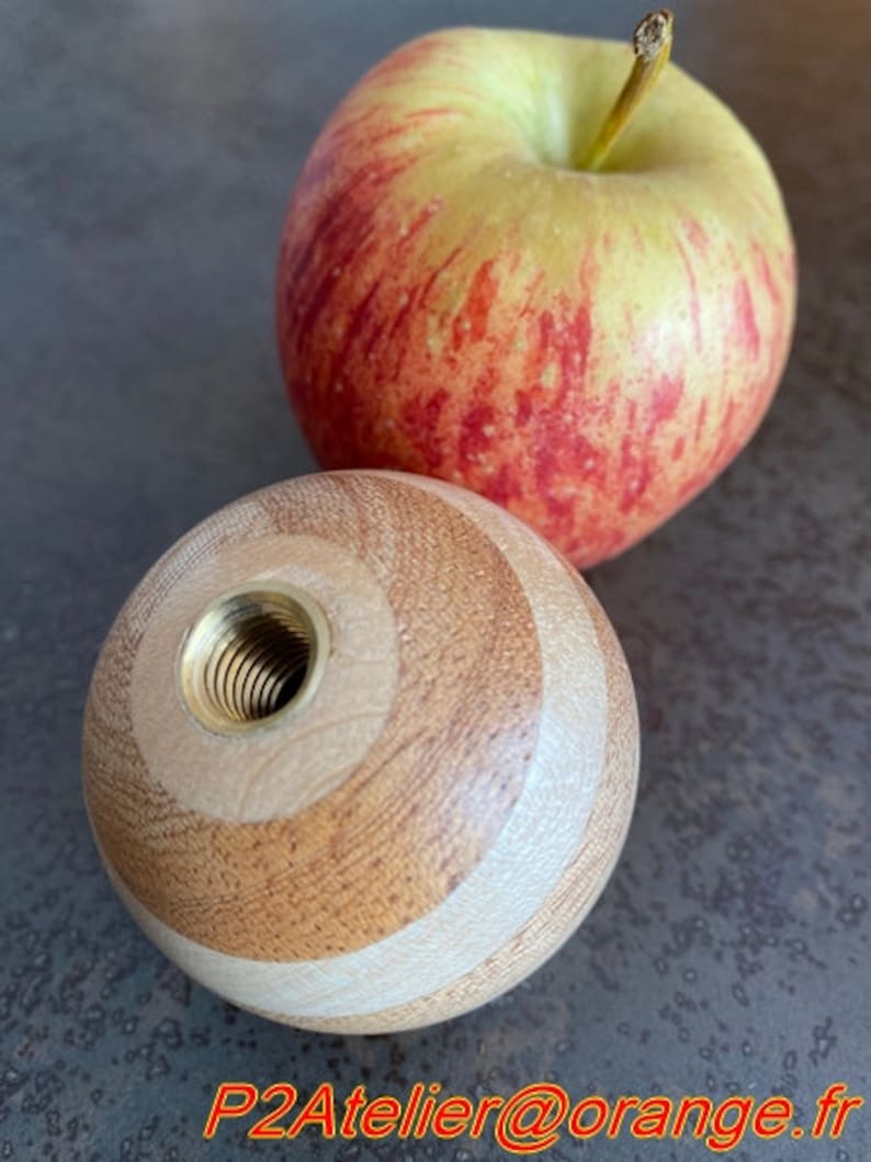 May include: A wooden knob with a threaded brass insert. The knob is made of light and dark wood and has a striped pattern.