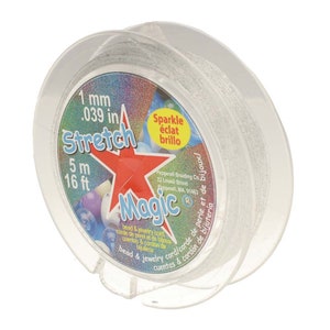 Puede incluir: Una bobina de cordón elástico transparente para cuentas y joyería de 1 mm (0,039 pulgadas) con brillo plateado. La bobina está etiquetada como "Stretch Magic" con una estrella roja y el texto "Sparkle éclat brillo".