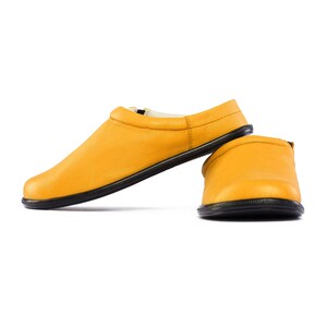 May include: A pair of yellow leather slippers with black soles. The slippers are laid out on a white background.