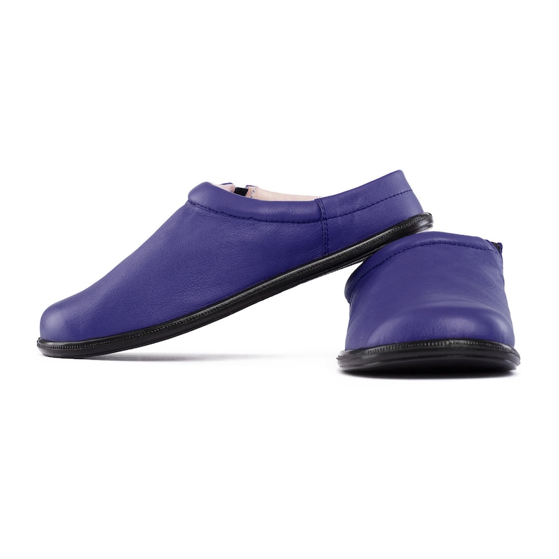 May include: A pair of blue leather slippers with a black sole. The slippers are laid out on a white background.