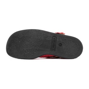 May include: The bottom of a red leather sandal with a black sole. The sole has the brand name "Truckers" printed on it.