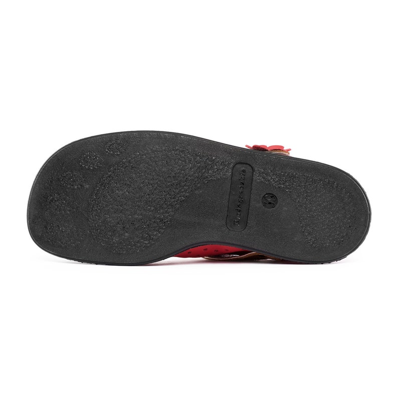 May include: The bottom of a red leather sandal with a black sole. The sole has the brand name "Truckers" printed on it.