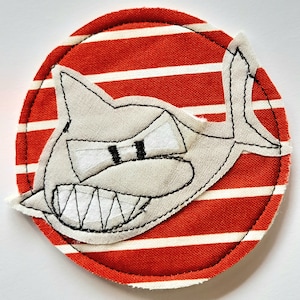 Könnte beinhalten: Ein weißer Hai mit einem zahnigen Grinsen ist auf einen roten und weißen gestreiften Stoffkreis appliziert.