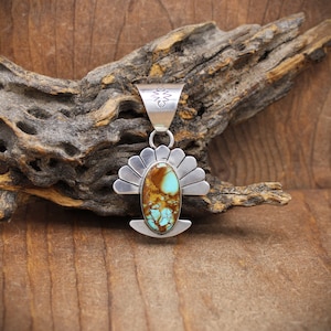 May include: A silver pendant with a turquoise stone set in a sunburst design. The stone is a mix of brown and blue.